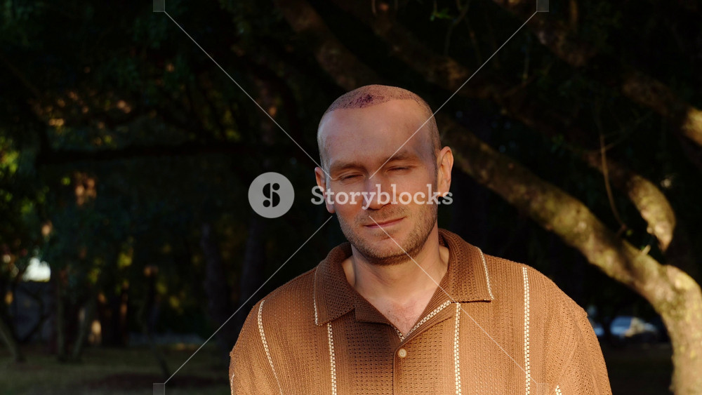 A portrait of a calm and content Caucasian man in a brown polo shirt, showing a healing scalp with scabs after a recent hair transplant