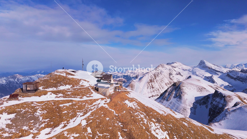 Hotel at the Top of Faulhorn Mountain on Sunny Winter Day. Thawed Patches of Grass. Snowy Swiss Alps. Switzerland. Aerial View. Orbiting