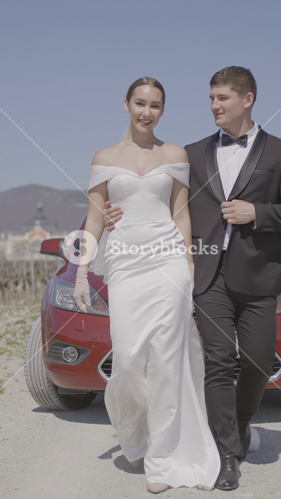 Newlyweds are walking beautifully in field. Action. Stylish newlyweds are hugging on road. Newlyweds in stylish outfits are walking epically