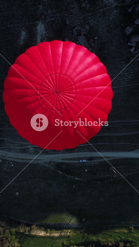 Aerial top view of a red hot air balloon floating over a mountain slope, a narrow path, and a green meadow. Shot. Concept of travelling and