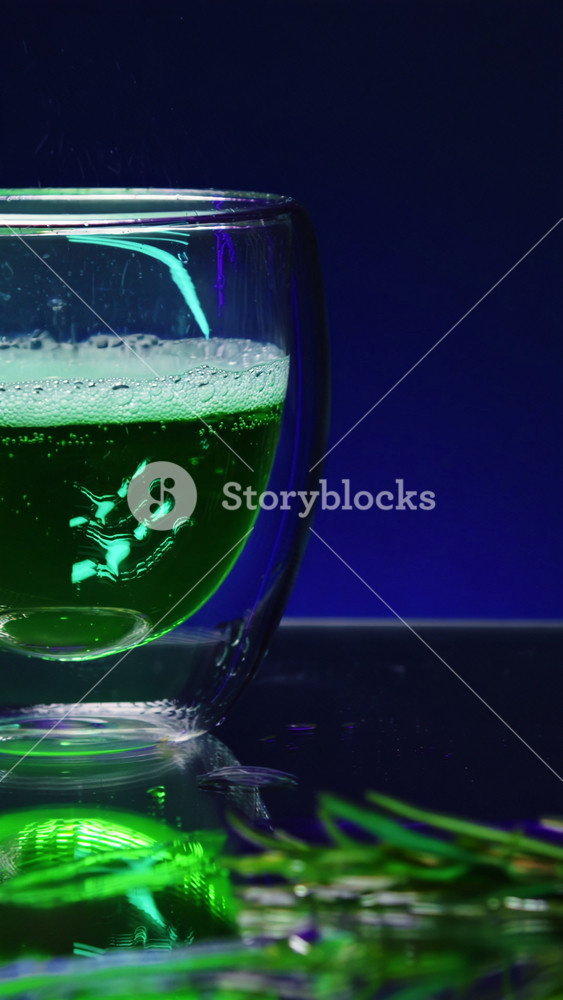 Close up of pouring green cocktail beverage in a transparent glass standing on bar counter. Stock clip. Bar counter decorated by green