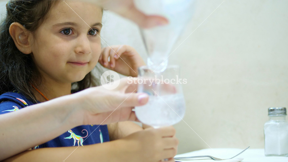 Young girl watching carbonated mineral water being poured into a glass. Dining lifestyle scene in an Italian restaurant.