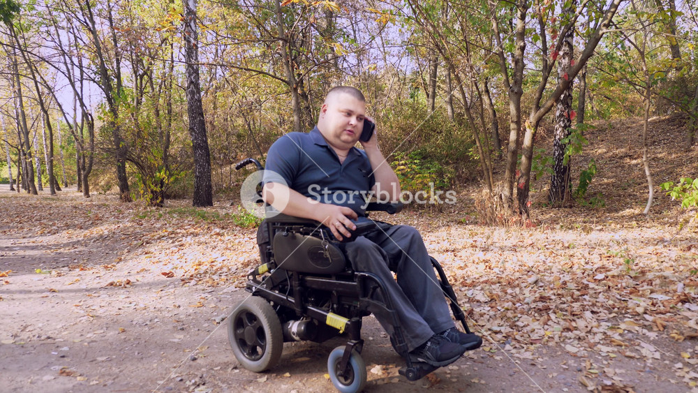 wheelchair man. Handicapped man. young disabled man rides in an automated wheelchair and talking on a cell phone, in a city park, on an autumn sunny day.