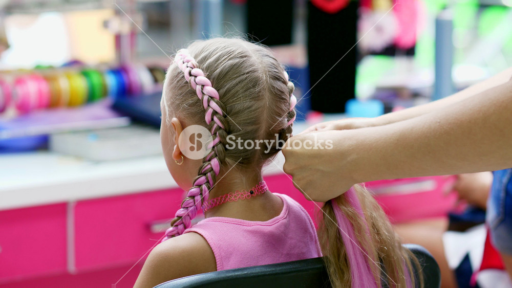 Process of professional hair styling for a little girl in modern beauty salon. Master braiding pink kanekalon into pigtails.