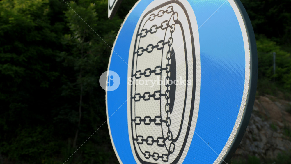 Close-up of a road sign mandating the use of anti-slip chains. Blue sign with wheel symbol in chains located in the Alps.