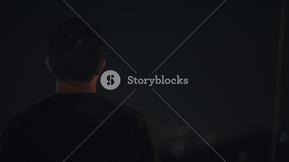 Cinematic footage of a man standing alone overlooking city lights at night. Urban night scene with soft bokeh lights, representing solitude, reflection, and emotional mood in a modern city environment.