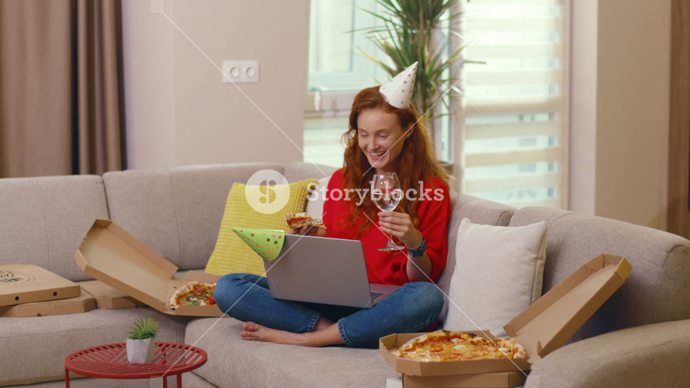 Birthday for one. Holiday celebration. Excited ginger funny woman drinking wine eating tons of pizza speaking to friend via laptop