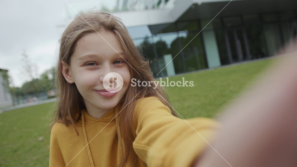 gorgeous portrait of a happy female schoolkid taking selfies outdoors in open area. close-up of cheerful girl smiling and waving hand on