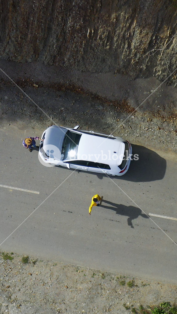 Aerial shot of couple with broken white car parking on highway, catching cars in the mountains during roadtrip. Car accident. Car breakdown
