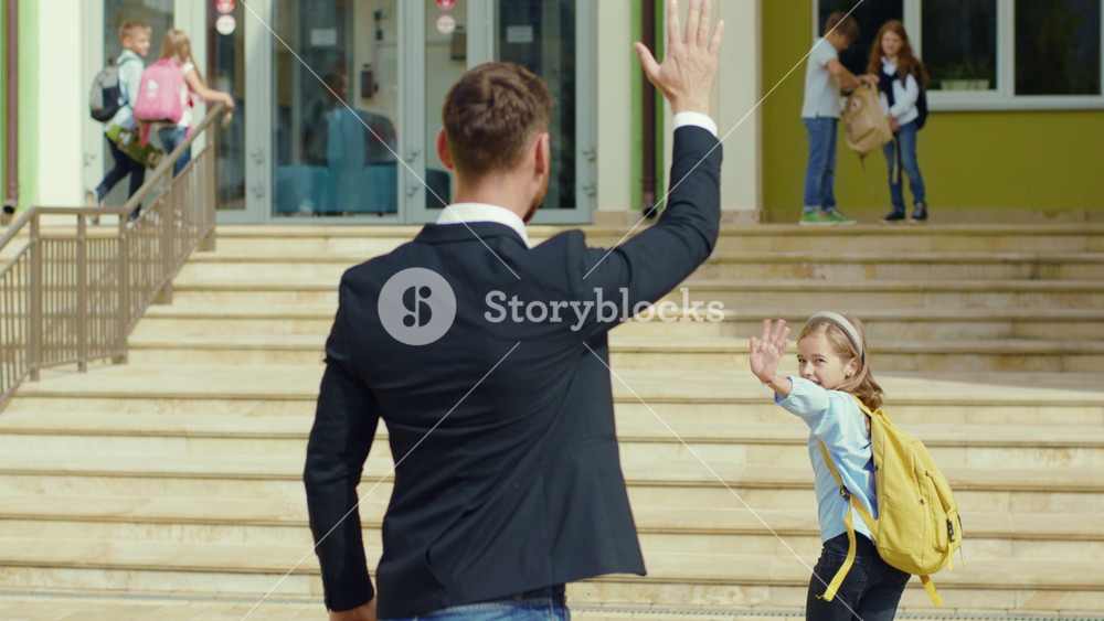 Caucasian father escorts his daughter to school and waving hand saying goodbye. Adorable little child girl hurrying for lessons running to