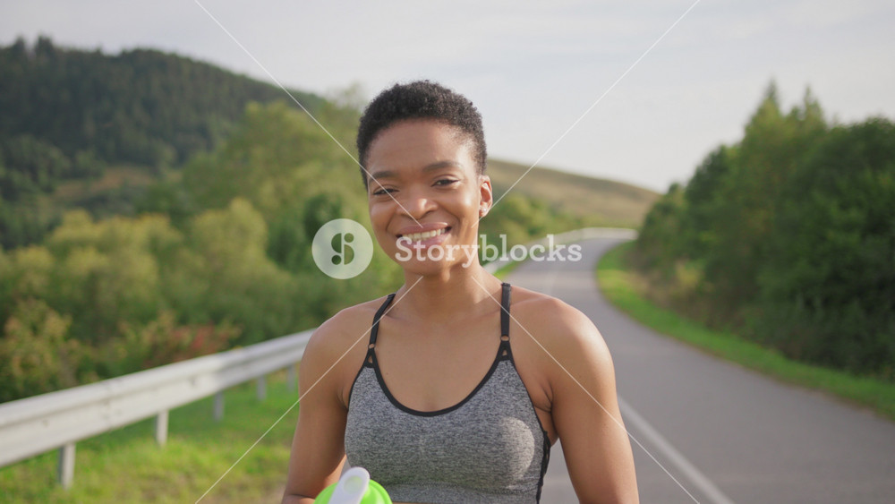 Portrait attractive strong young afro-american beautiful healthy girl runner woman smiling holding sports cup outside. Fitness woman