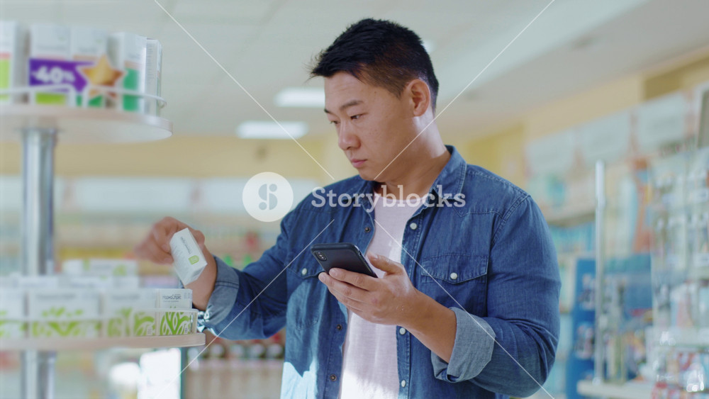 NEW YORK - April 5, 2020: Attractive young asian man with looking at medication in the pharmacy use phone. Health buying happy friendly