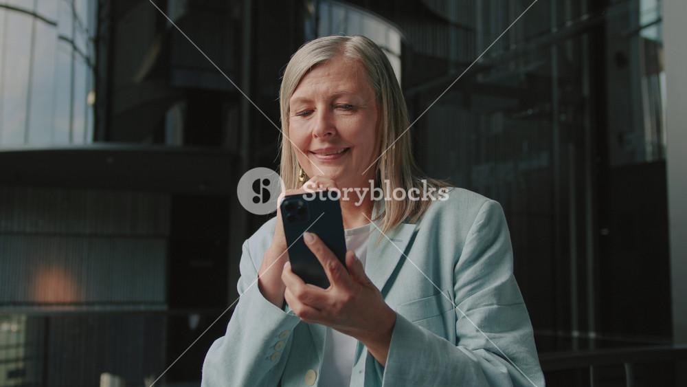 Footage of thoughtful confident smiling blonde 60s woman using smartphone and chatting with husband. Attractive fashionable businesswoman in
