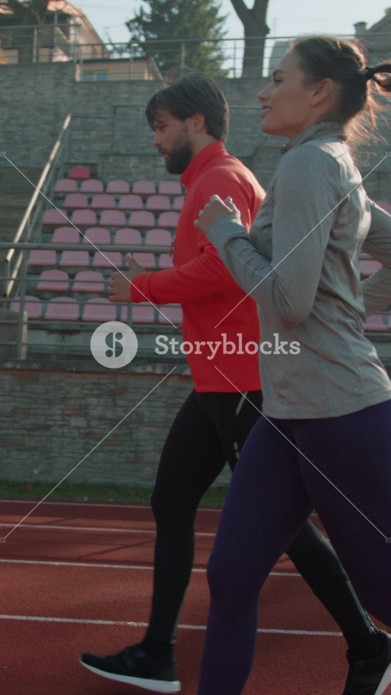 Couple engaged in morning exercise on outdoor track, Man and woman run together on red track in morning sunlight