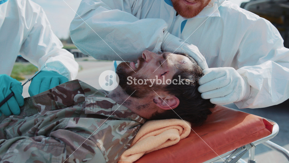 Close-up footage of men in uniforms for field doctors providing first aid, cleaning of wounds of military man lying on stretcher. Team work