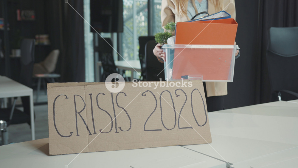 Crisis 2020 banner. Young woman quitting job collecting her personal items in box by working desk leaving the office corporate. Business