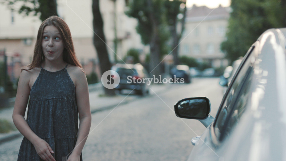 Good-looking young girl walking down street full of autos. Female teenager opening door of strange parked car. Outdoors. Summer.