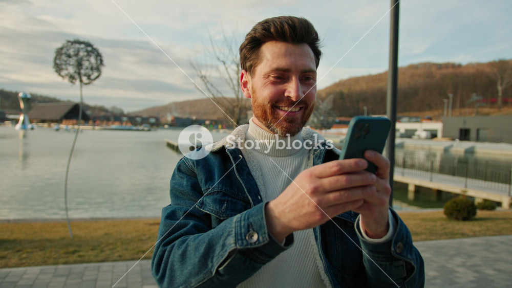 Funny young man in stylish jacket use typing on phone smiling feel happy. On the background of the wonderful buildings in sunny day