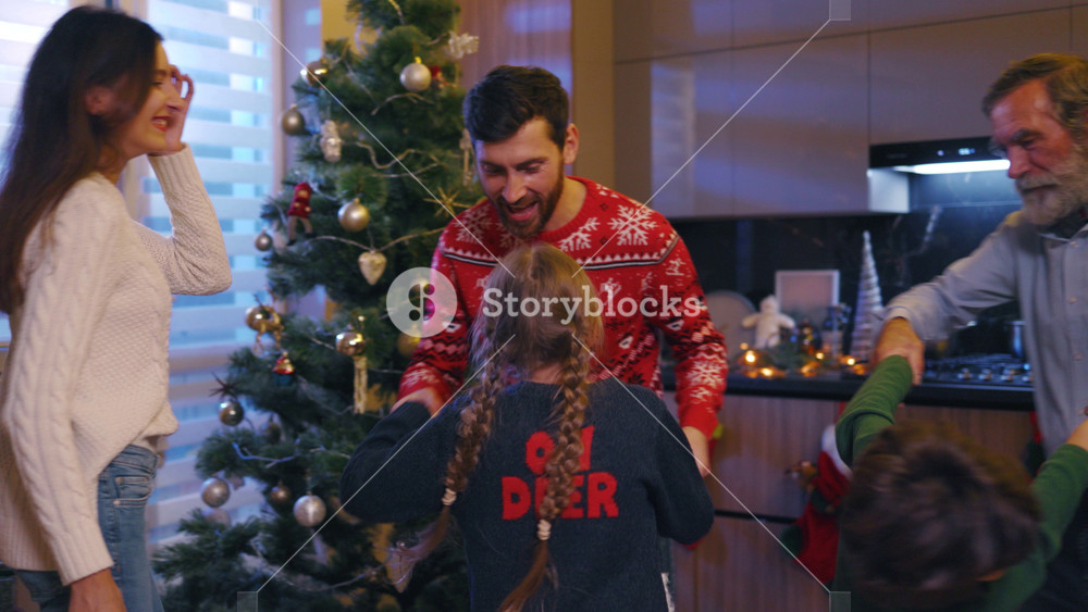 Affectionate young family with grandpa and couple children dancing celebrating merry christmas near decorated tree. Home party. Reunion