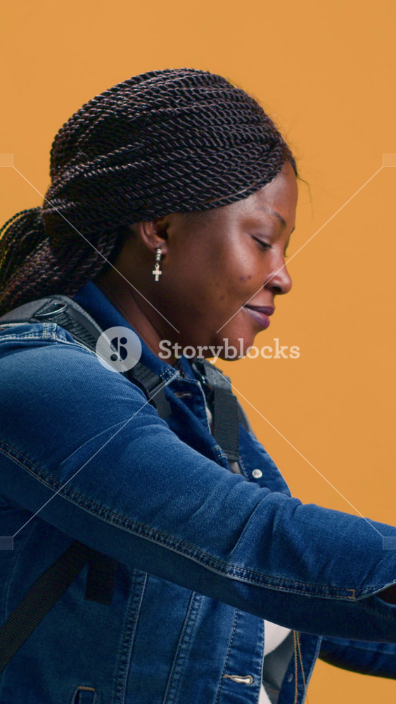 vertical video Reliable african american delivery person with bag on the back delivers food to urban neighbourhood. Active black woman using
