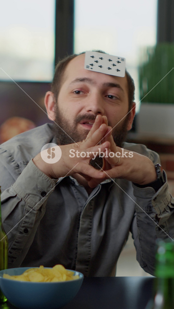 Vertical video: Multiethnic group of people laughing together at board games play with cards in living room. Positive men and women having