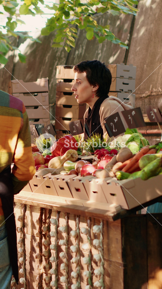 Vertical video: Diverse team of sellers helping customers choose natural products, selling homegrown eco fruits and vegetables. Local vendor