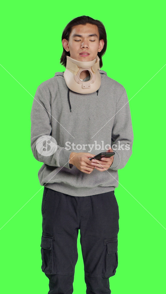 Front view of young adult with neck collar answers call on smartphone, talking to people about his bone fracture accident. Hurt person