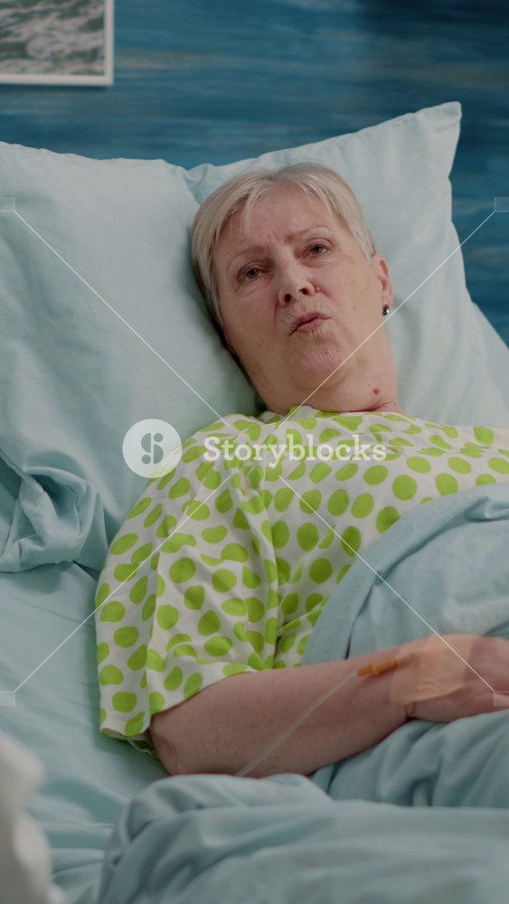 Vertical video: Doctor doing healthcare consultation with retired patient in bed at nursing home. Aged woman with illness talking to