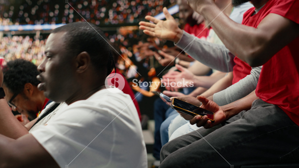 Tense sports fans checking online betting odds and cash out options on smartphone, live football match in the stadium stands. Passionate