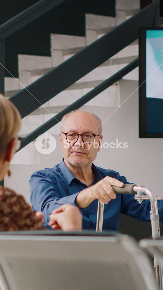 Vertical video: Senior people sitting in waiting area at health clinic, talking about medicine and healthcare appointments. Old man with