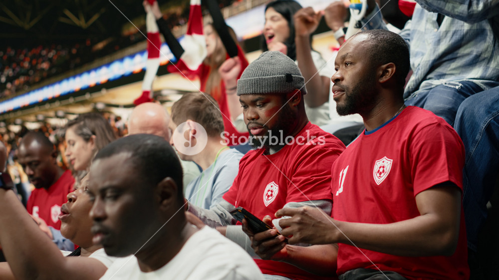Football fans placing a risky bet ticket on in-play live gambling app, watching intense soccer match from the stadium stands. Enthusiasts
