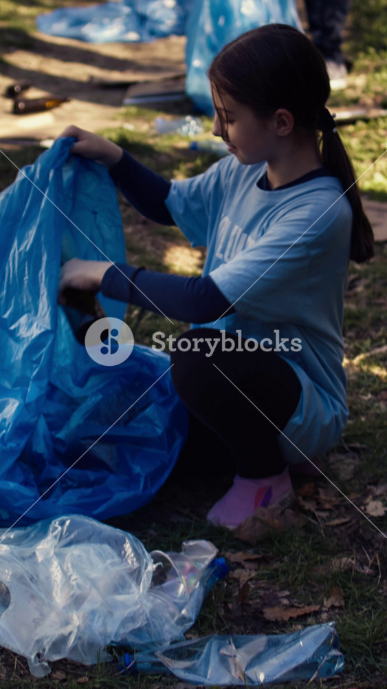 Tired little girl collecting trash and plastic bottles from the forest, helping the volunteers with litter cleanup. Child activist picking