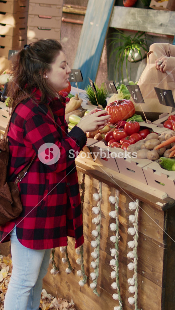 Vertical video: Happy seller talking to client and selling seasonal locally grown veggies at farmers market. Local vendor helping consumer