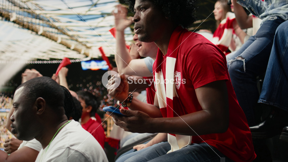 Black football fan with wig monitor live betting odds at stadium during live soccer match filled with cheering and crowd excitement