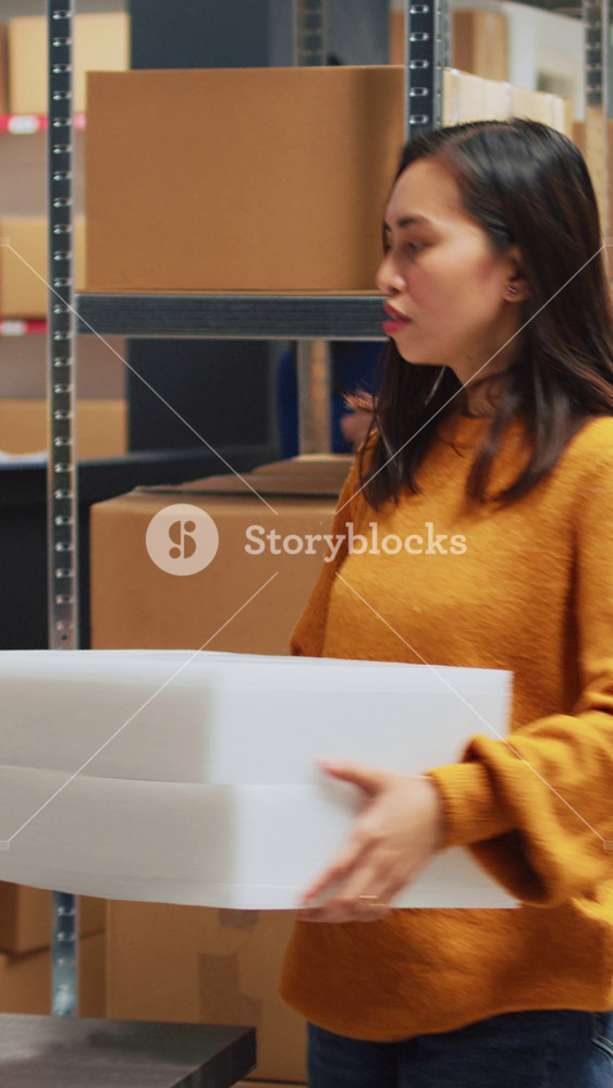 Vertical video: Male employee in wheelchair looking at stock goods, checking merchandise in packs with woman colleague. Asian man with