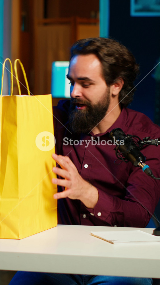 Vertical video Excited media star holding colorful shopping bags, showing fans purchases, filming himself in apartment. Playful content