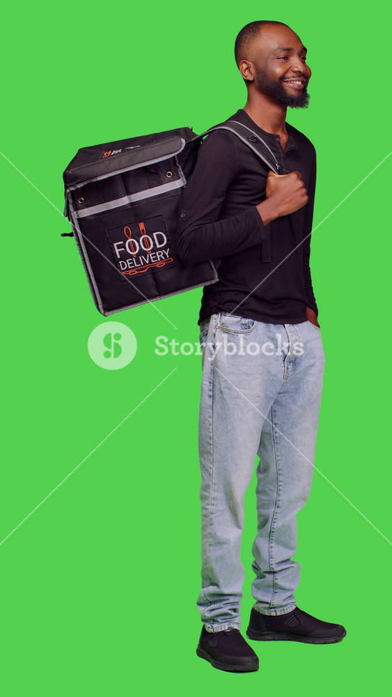 Vertical video: Side view of african american person working as deliveryman on camera, carrying thermal bag to deliver fast food. Male model
