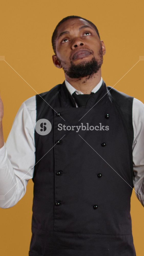 Vertical Video Spiritual waiter in apron praying to Jesus Christ with belief, being hopeful for good luck against yellow background
