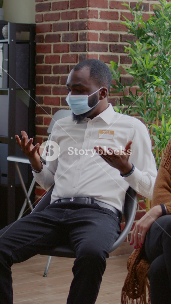Vertical video: African american man talking to group of people at aa therapy meeting about addiction during pandemic. Person with face mask
