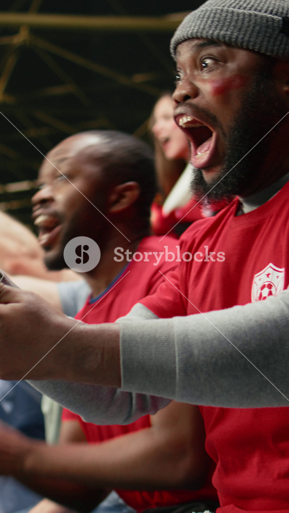 Vertical Video Excited football supporter celebrating live bet win on his phone, dramatic soccer match in a stadium. Happy fan reacts with