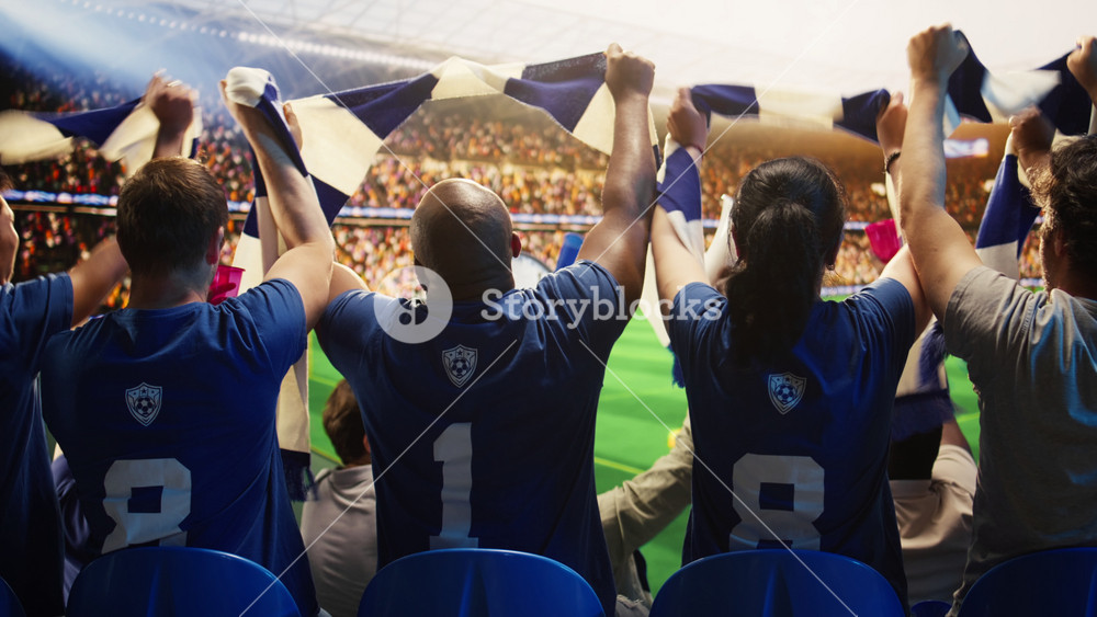 Close up of happy soccer fans lifting scarves in crowded stadium to team support. Cheerful football supporters waving scarves, chanting