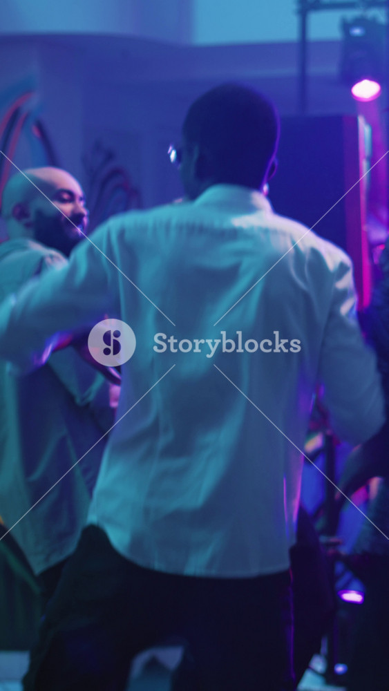Vertical video: Group of friends enjoying party at club, dancing on modern music and jumping on dance floor. Young people feeling happy and