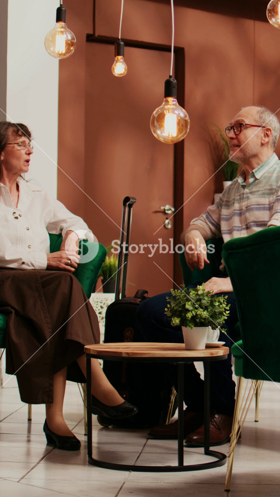 Vertical Video Bellboy serving cup of coffee to people waiting in lounge area, senior couple travelling abroad to see historical landmarks
