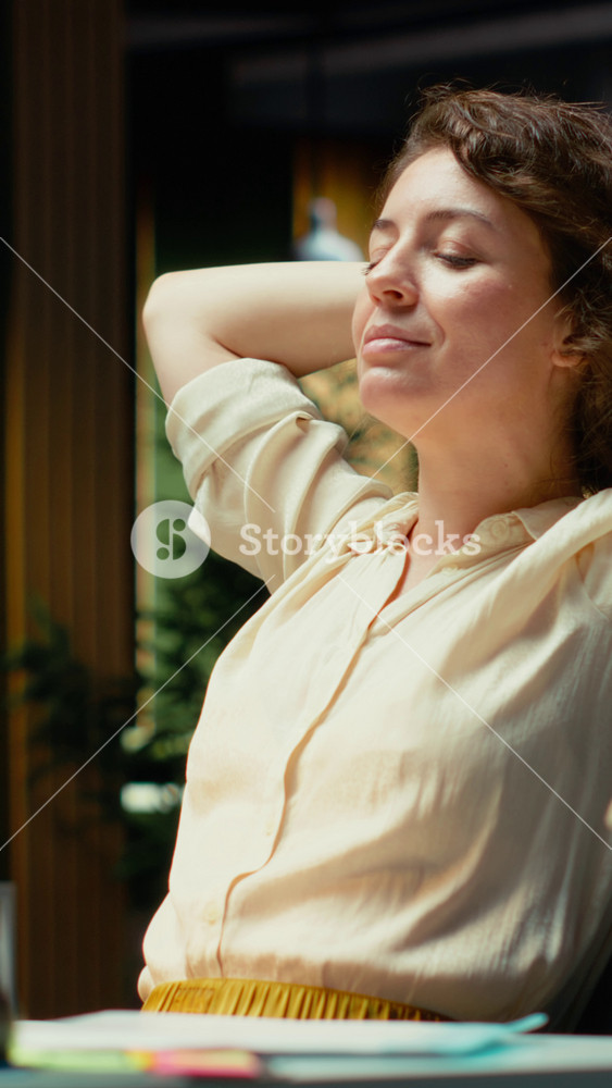 Vertical Video Pleased businesswoman enjoys a quiet moment of downtime in a corporate setting, reclining in her chair with comfortable laid