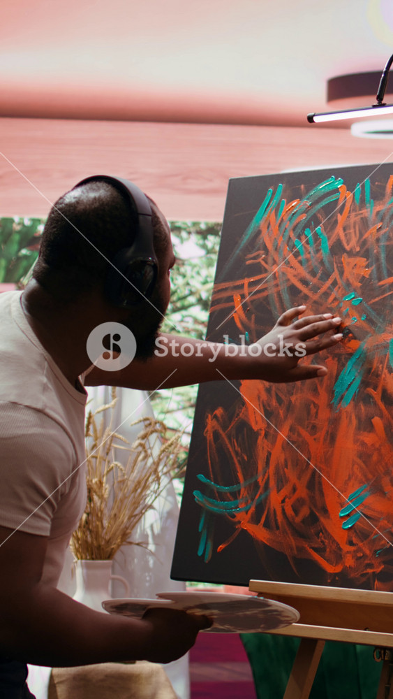 Vertical Video Artist listening to music and creating an abstract painting with his fingers, showing his skills and contemporary ideas in