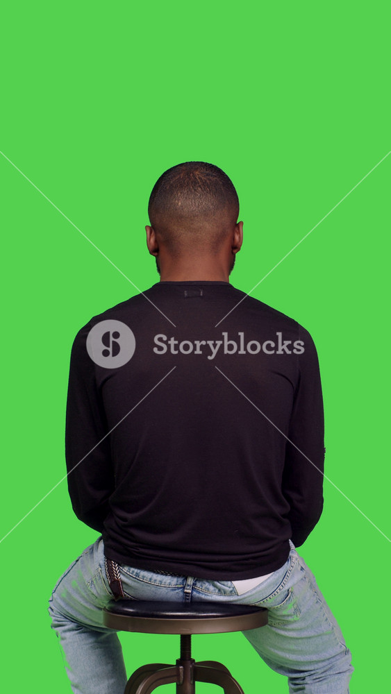 Vertical video: Back view of young happy person on chair sitting and waiting, feeling positive and relaxed with stylish jeans and shirt