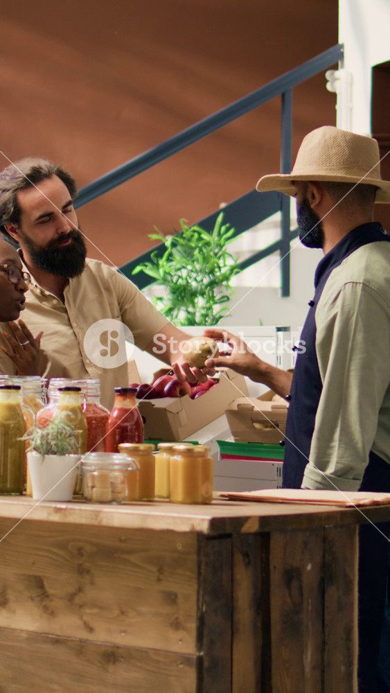 Vertical video Merchant shows fresh produce to people in local zero waste market, seller recommending homegrown fruits and veggies. Young