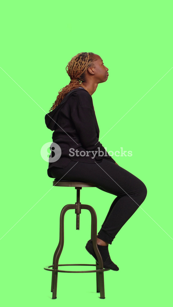 Vertical video: Young confident adult sitting on chair over full body green screen, waiting in line and preparing. Relaxed female adult sit