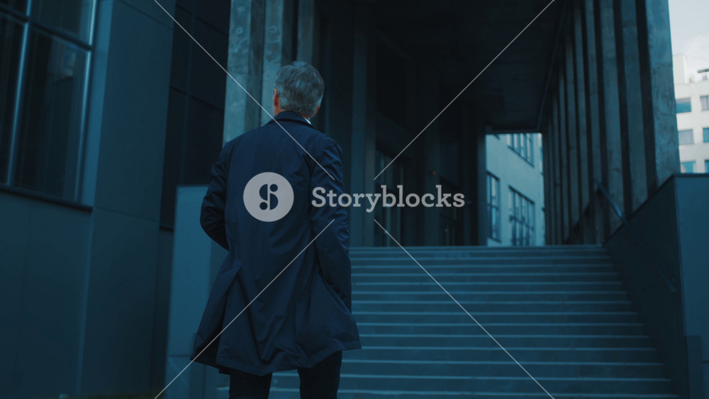 Grey-haired mature adult businessman wearing long autumn coat walking on street entering office campus district outside. Business people.