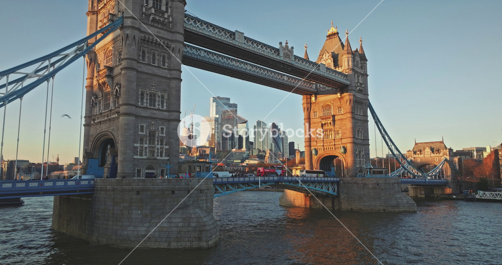 London: Tower Bridge against a backdrop of modern skyscrapers city during sunset, boats sailing on the River Thames and bus crossing the